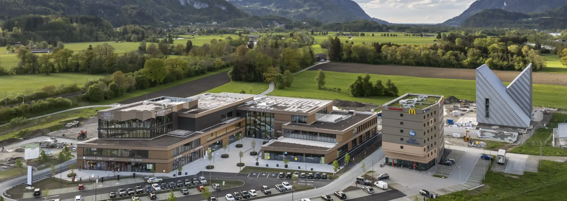 Luftaufnahme des Kaiserreichs mit umliegenden Geschäftsgebäuden, Parkplätzen und Alpen