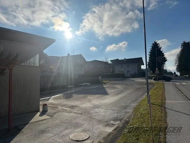 Asphaltierte Freifläche neben der Straße, mit Wohnhäusern im Hintergrund