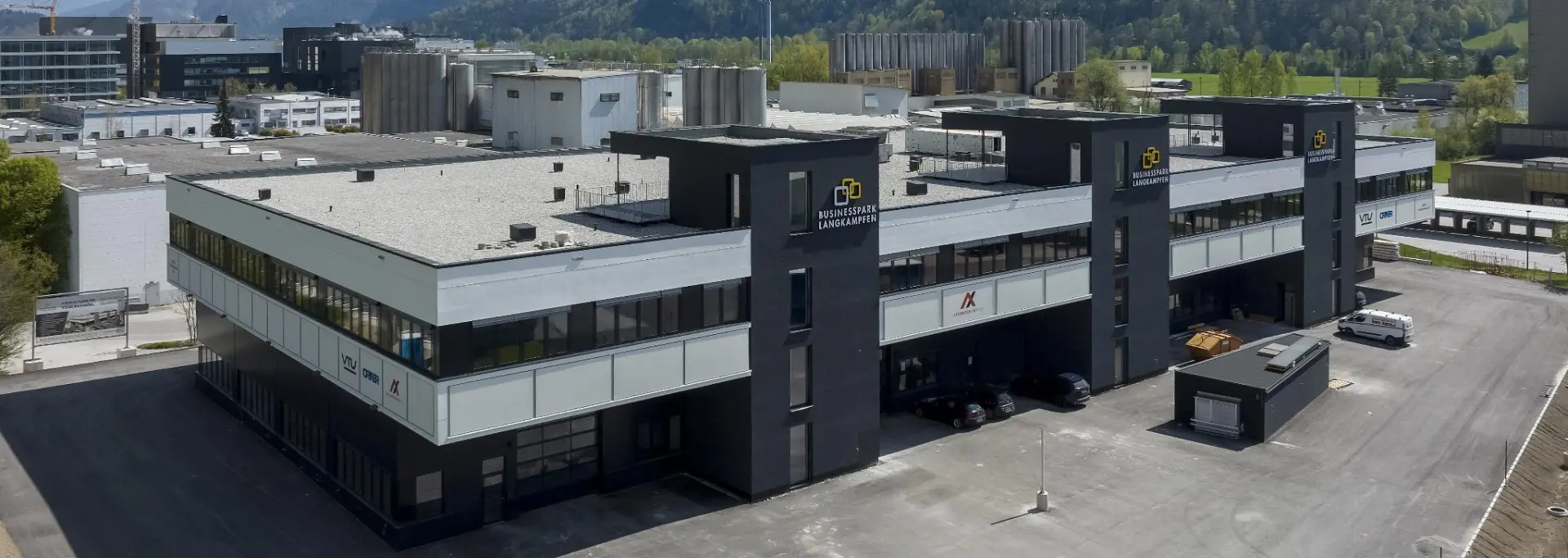 Außenansicht des Businessparks Langkampfen mit asphaltierter Fläche und Berge im Hintergrund